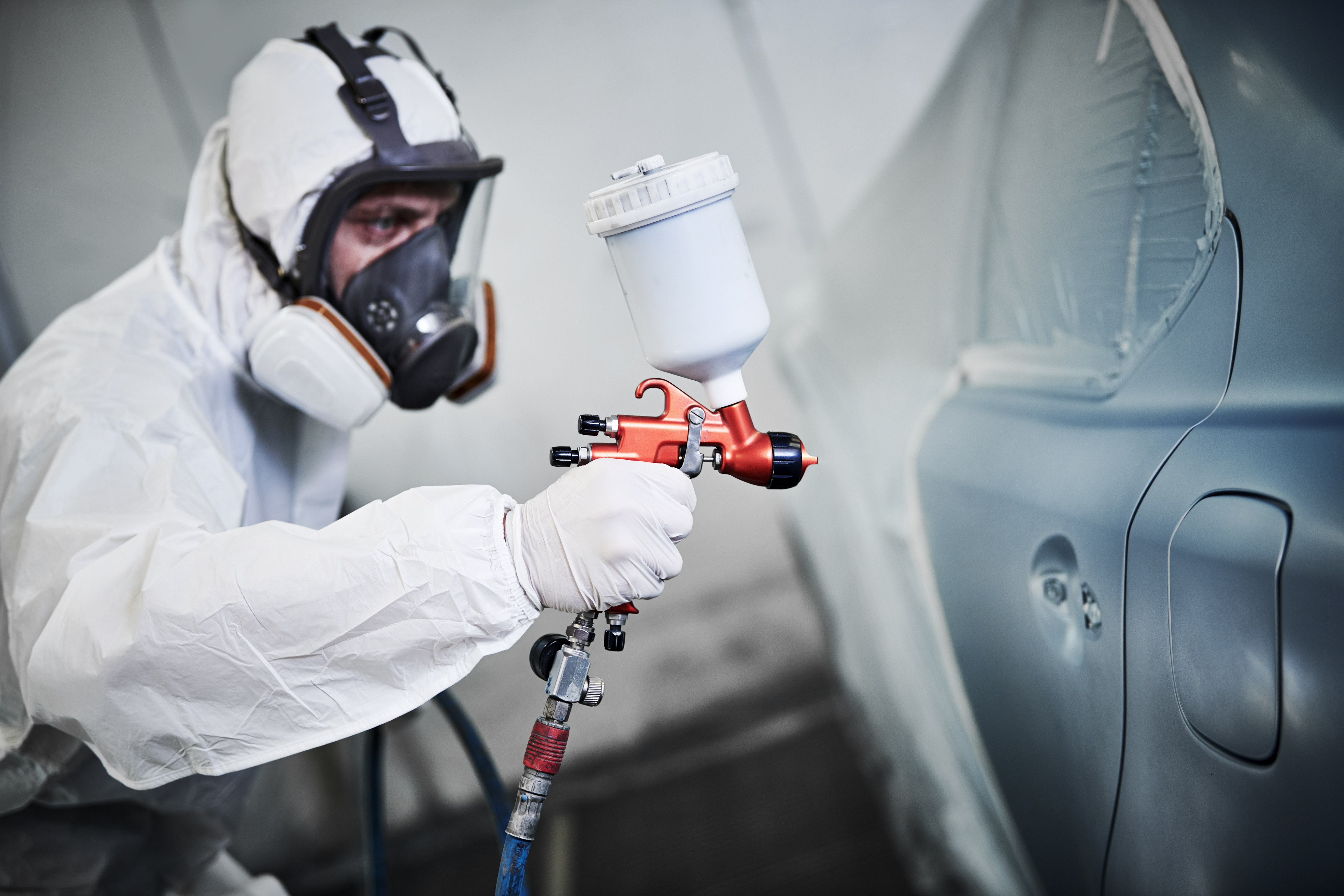 A painter refinishing the side panel of a grey car