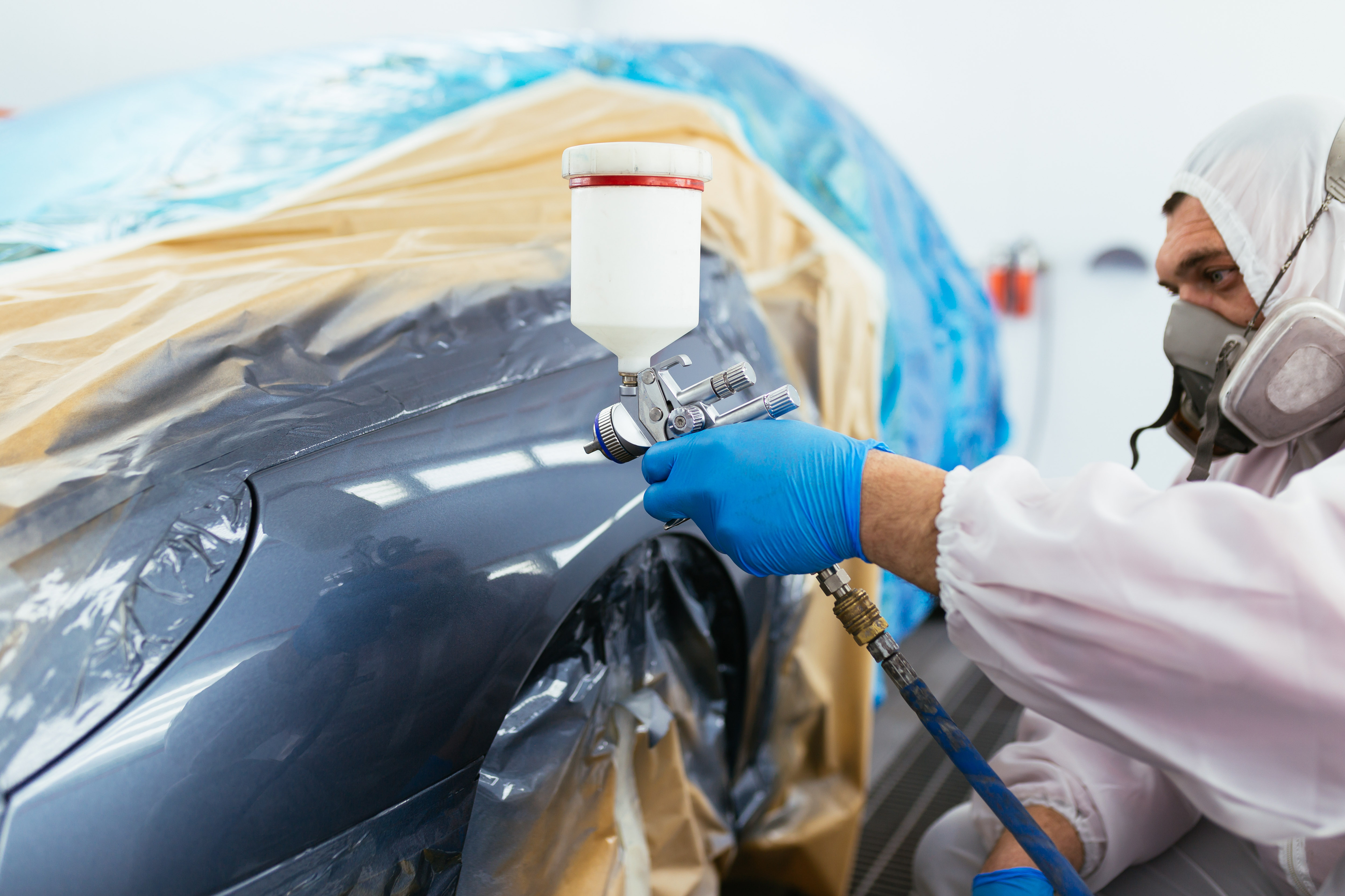 A painter spraying a masked grey car wing